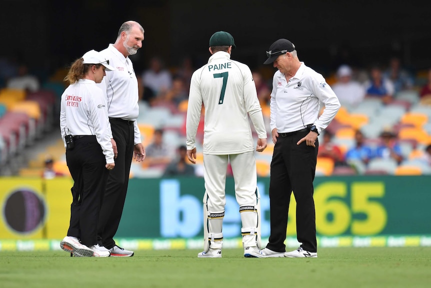 Tim Paine speaks with three match officials out in the middle of the Gabba during a rain delay.