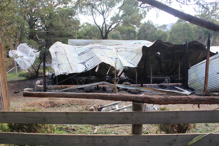 Twisted corrugated iron sits above a burnt-out home.