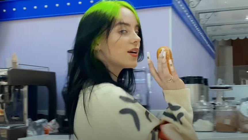 Billie Eilish holding a donut in profile in a still from the 'therefore i am' 2020 music video