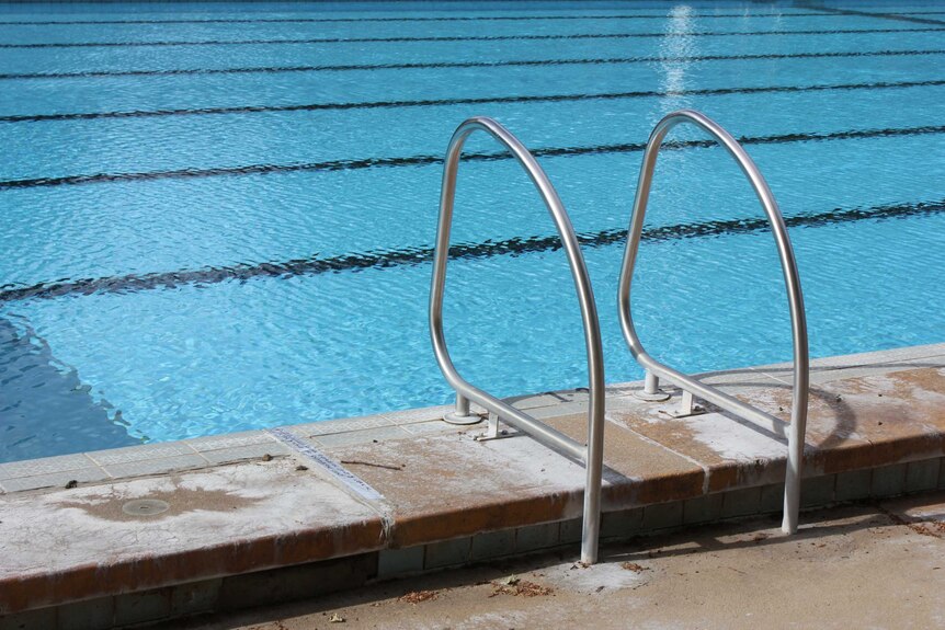 A steel ladder on the side of an outdoor pool.