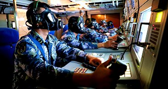 Sailors wearing gas masks operate a combat direction system console aboard the amphibious dock landing ship Changbaishan.