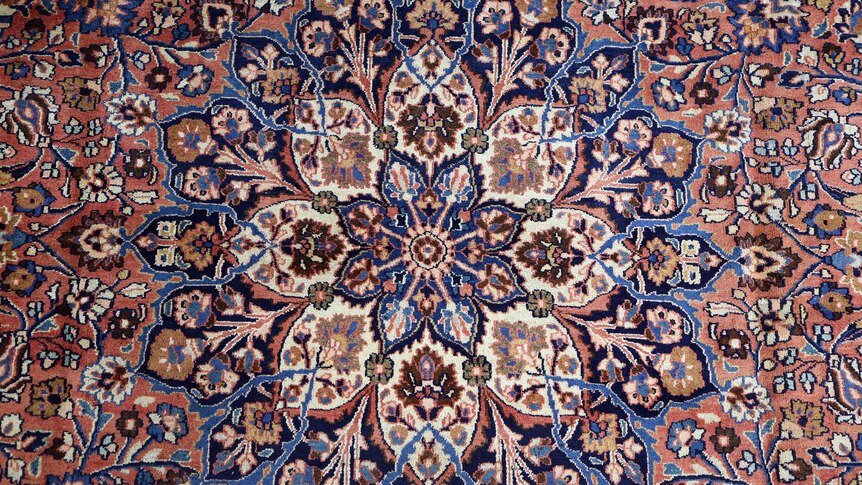A Persian rug design shows red, beige and blue flowers flowing outwards.