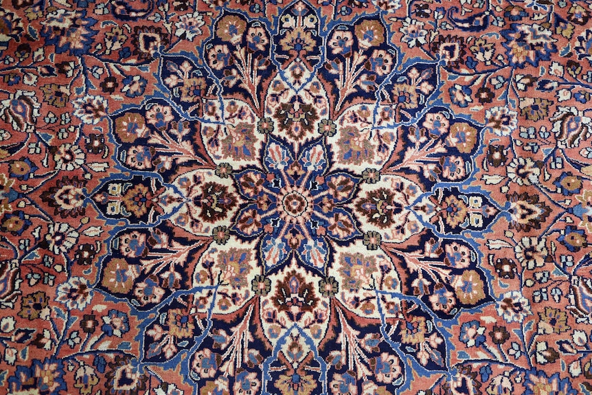 A Persian rug design shows red, beige and blue flowers flowing outwards.