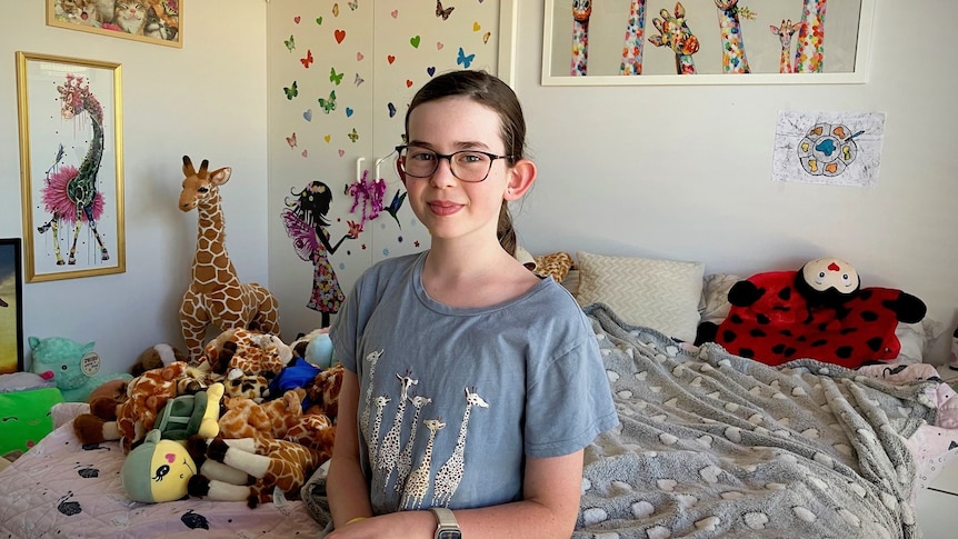 Thalia Keenan in her bedroom surrounded by soft toys, mainly giraffes.