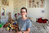 Thalia Keenan in her bedroom surrounded by soft toys, mainly giraffes.