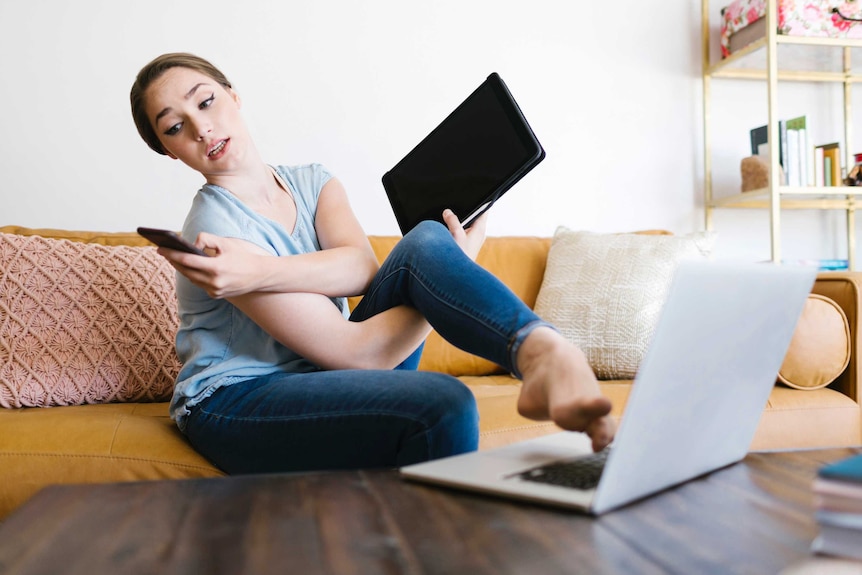 Woman holding an ipad, laptop and phone all at once.