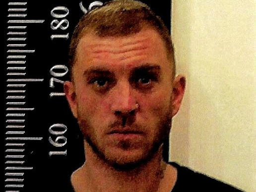 A mug shot of a 29-year-old man with dark hair who wears a serious expression