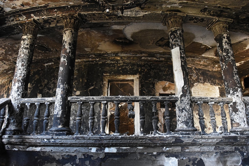 A once-white ornate interior balcony is burned black and covered in debis