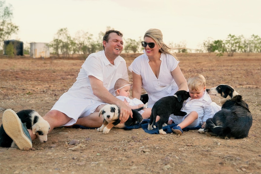 A man and woman dressed in white for family photos sit with young children and dogs