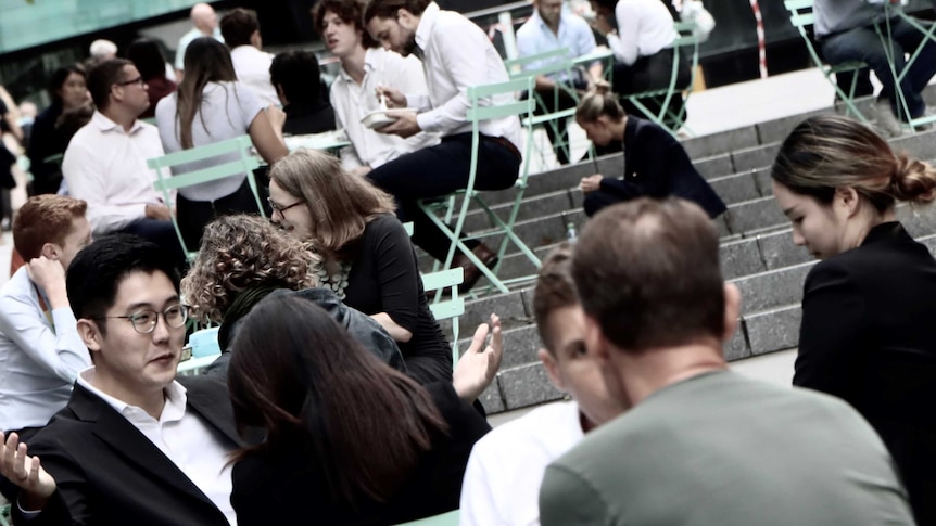 Men and women in business attire sit at an outdoor cafe.