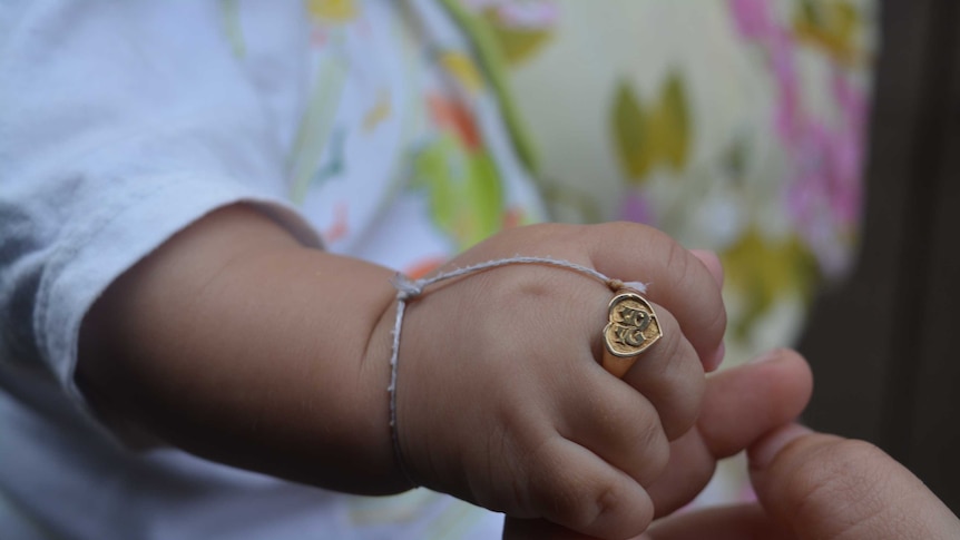 A close-up shot of a gold-coloured ring, imprinted with the Khmer script for the letter S, on the baby's finger.