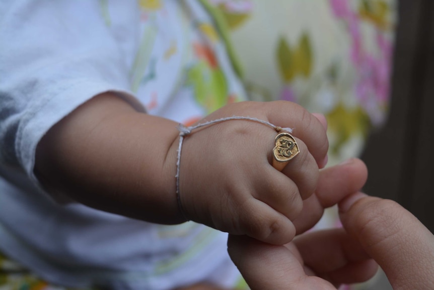 A close-up shot of a gold-coloured ring, imprinted with the Khmer script for the letter S, on the baby's finger.