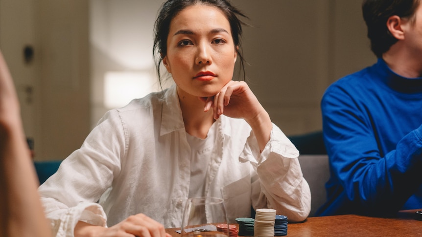 A woman sitting at a table playing poker and staring straight ahead with no expression.