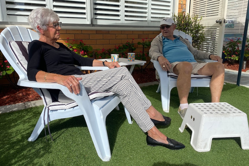 An elderly couple sit on garden furniture enjoying a cup of tea.