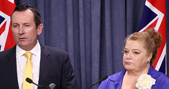 Mark McGowan and Sue Ellery stand at a lectern with flags in the background