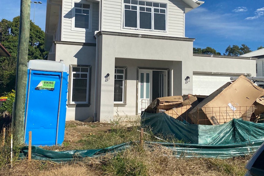 an unfinished partially-built home on a suburban street, large piles of rubbish and carboard are piled outside