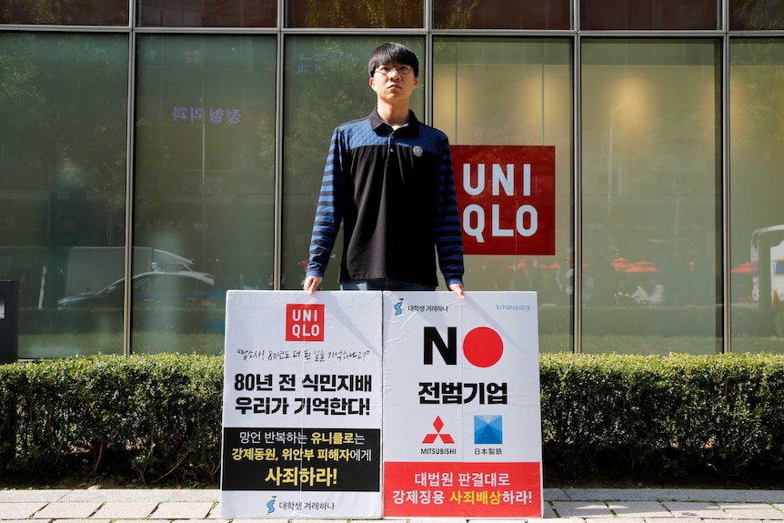 A student stands in front of a Uniqlo shop with protest signs.