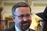 A close-up of Sebastian Gorka wearing a suit smilies while talking to two men either side of him