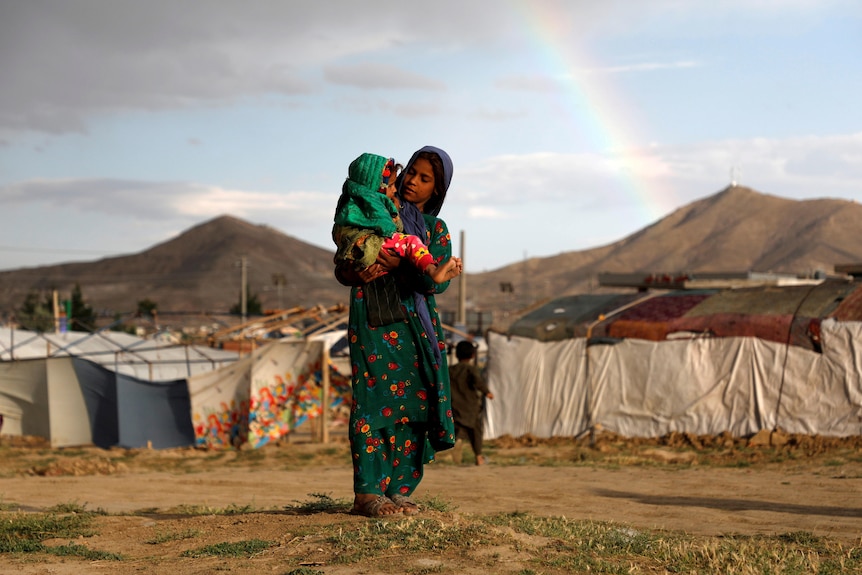 A woman in a long dress wearing a hijab holds a baby.