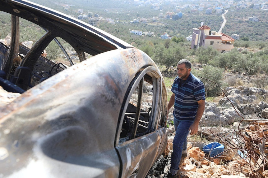 A Palestinian man stands near a burnt out car near Salfit in the West Bank