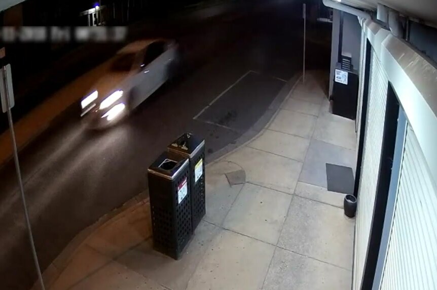 A still from CCTV footage shows a blurry image of a white sports car driving down the road.