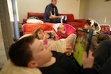 Three children sit and play on electronic devices.