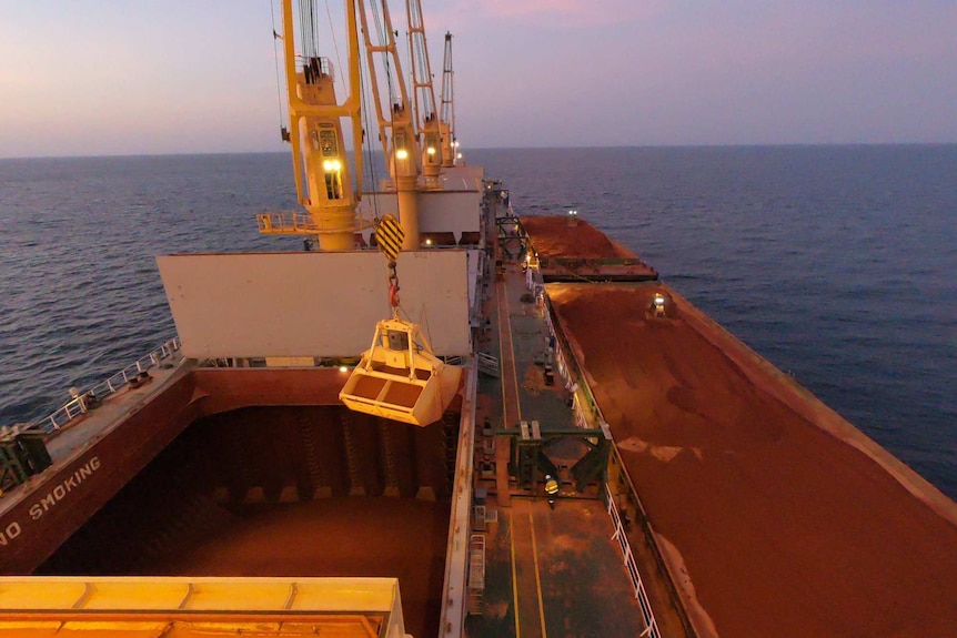 Large ship carrying red bauxite on ocean at dusk.