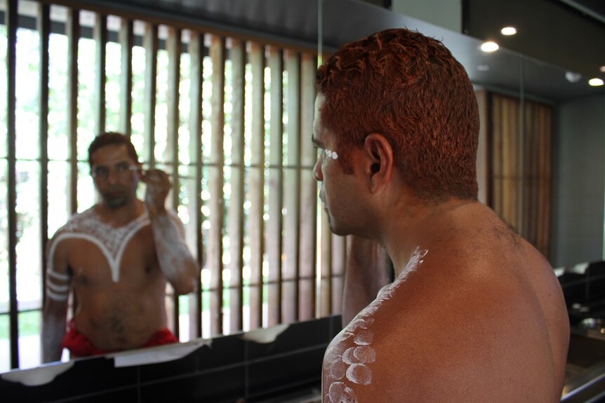 A photo of Weika painting his face before a performance showing his reflection in the mirror
