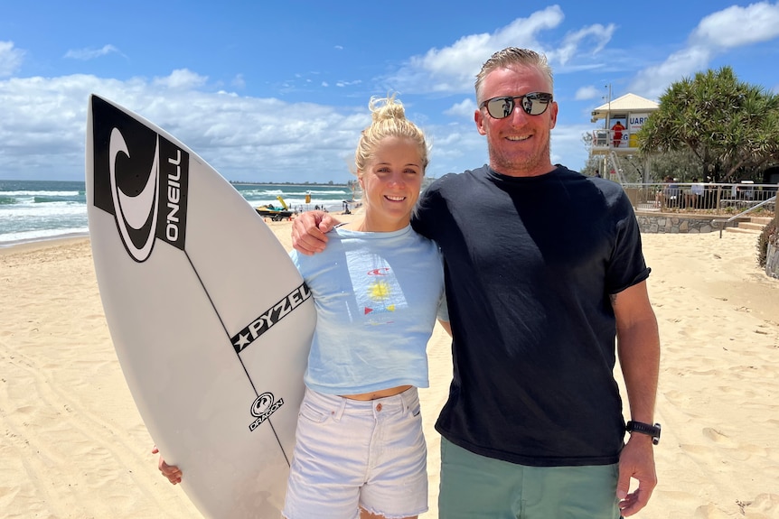 Woman on beach holding surfboard with male coach