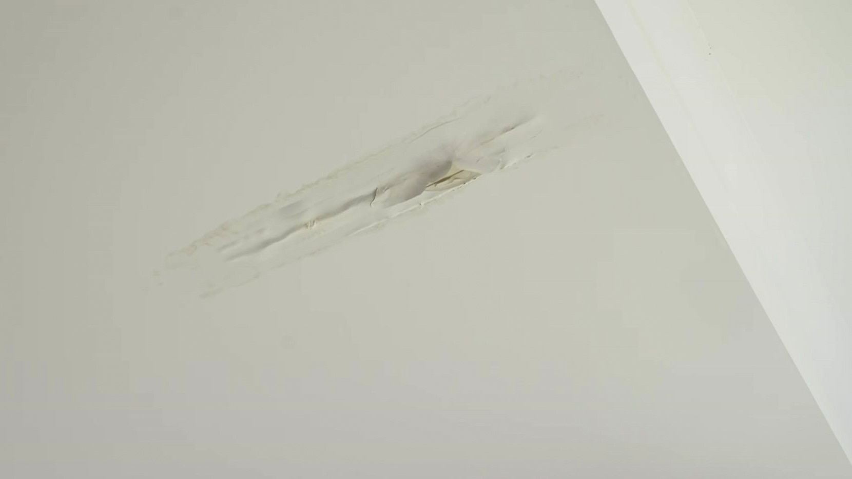 A white ceiling with a long hole in it and paint coming away due to a leak.