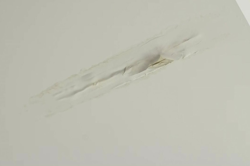 Un plafond blanc avec un long trou et de la peinture qui s'enlève à cause d'une fuite.