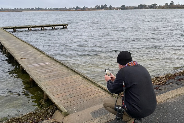 Man bending down to photograph jetty with phone