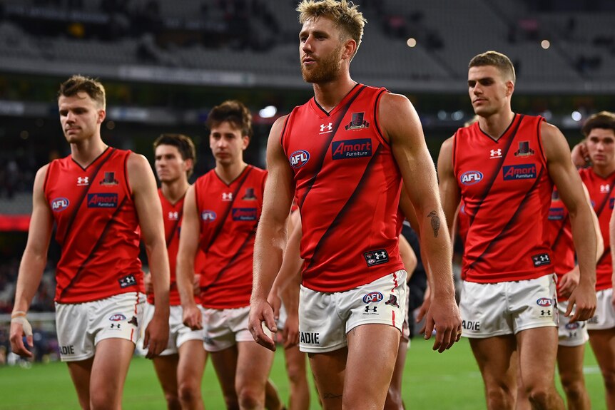 Dyson Heppell purses his lips as he leads disappointed Essendon players off the field