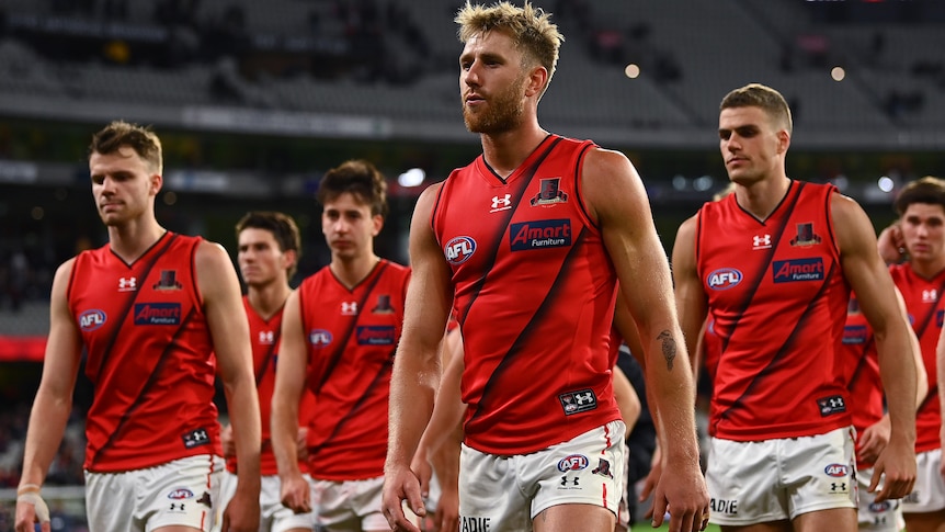Dyson Heppell purses his lips as he leads disappointed Essendon players off the field