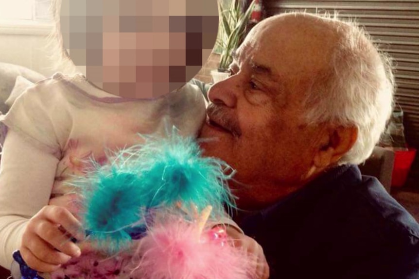 An elderly man holds a small child with a fluffy toy