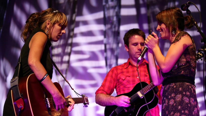 Three members of The Waifs performing on stage. Two with guitars, one holds a microphone.