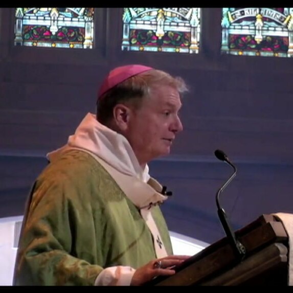 man in catholic garbs speaking at a church podium