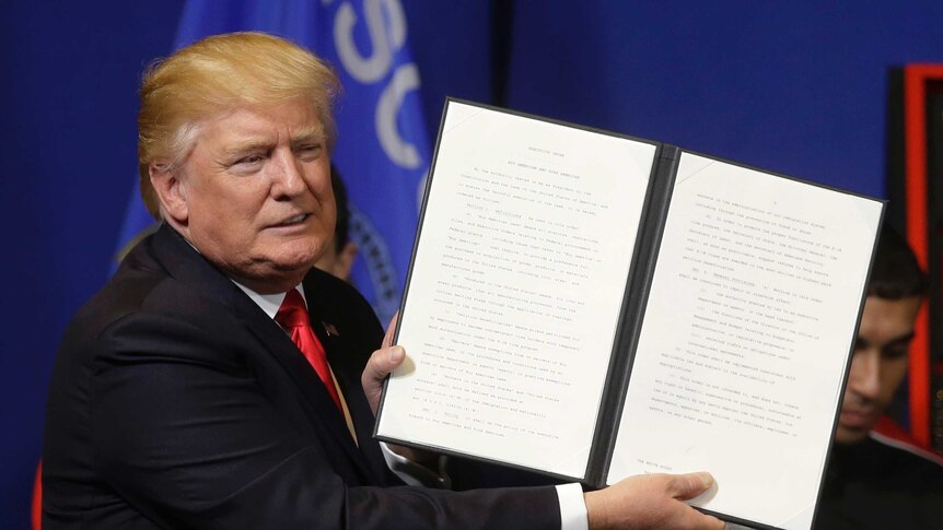 US President Donald Trump holds the executive order prior to signing it at a media conference.