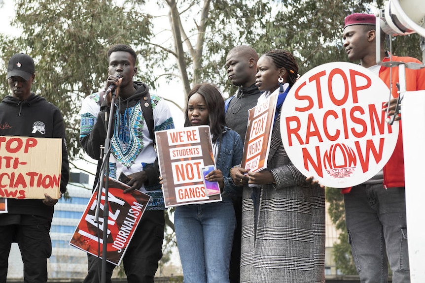 Group of men holding up Stop Racism now cards 