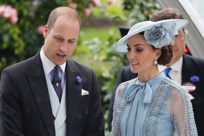 Duchess of Cambridge wears a powder blue dress and hat and stands next to Prince William who is wearing a morning suit
