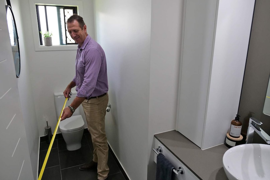 A man holds a building measure in a toilet room, to check the distance between the toilet door and the pan.