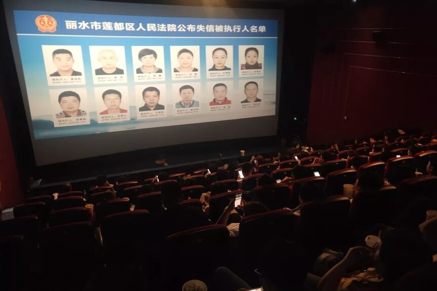 A movie theatre showing pictures of debtors on the big screen.