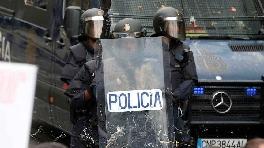 Spanish police in helmets hold a shield.