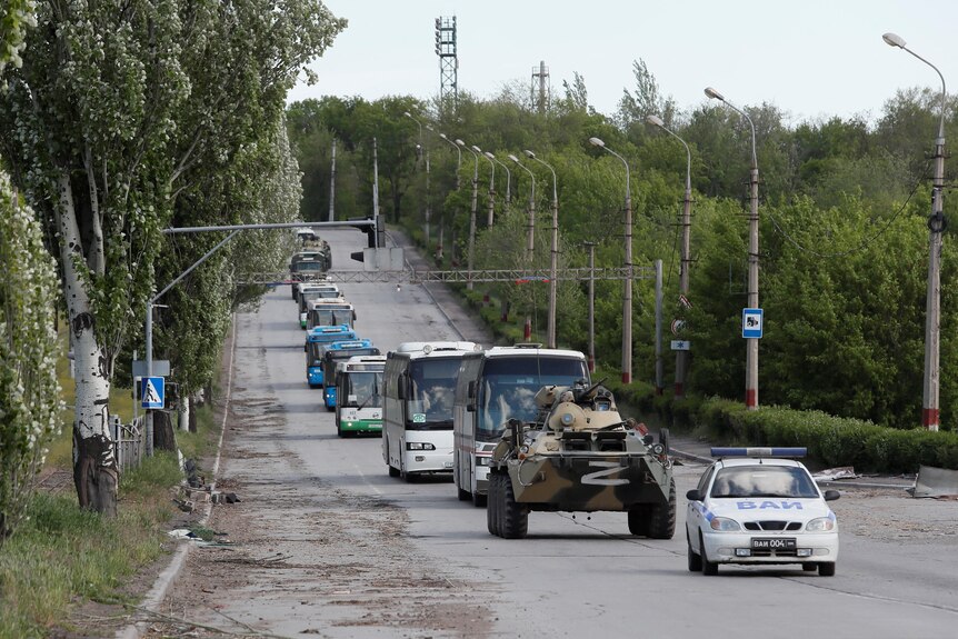 A convoy of buses, a tank and a car drive down a road carrying Ukrainian fighters.