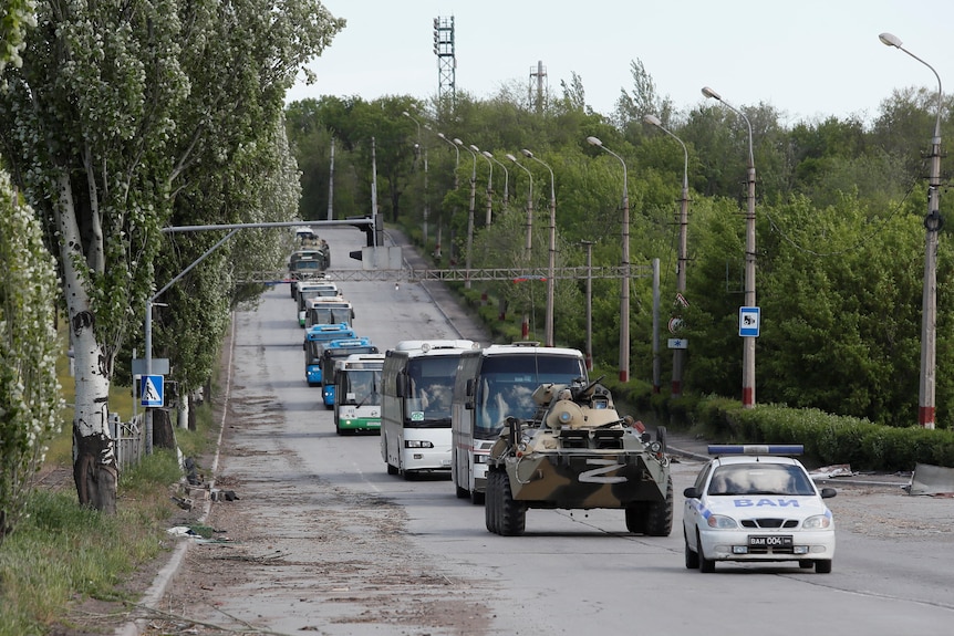 Un convoi de autobuze, un tanc și o mașină care circulă pe un drum în care se transportă luptători ucraineni.