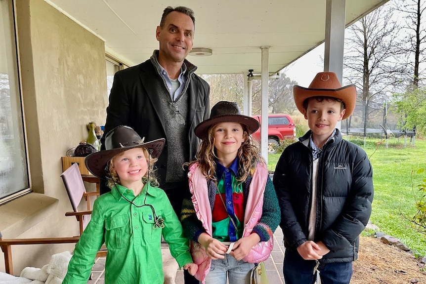 Man standing with three children, all of whom are wearing cowboy hats.