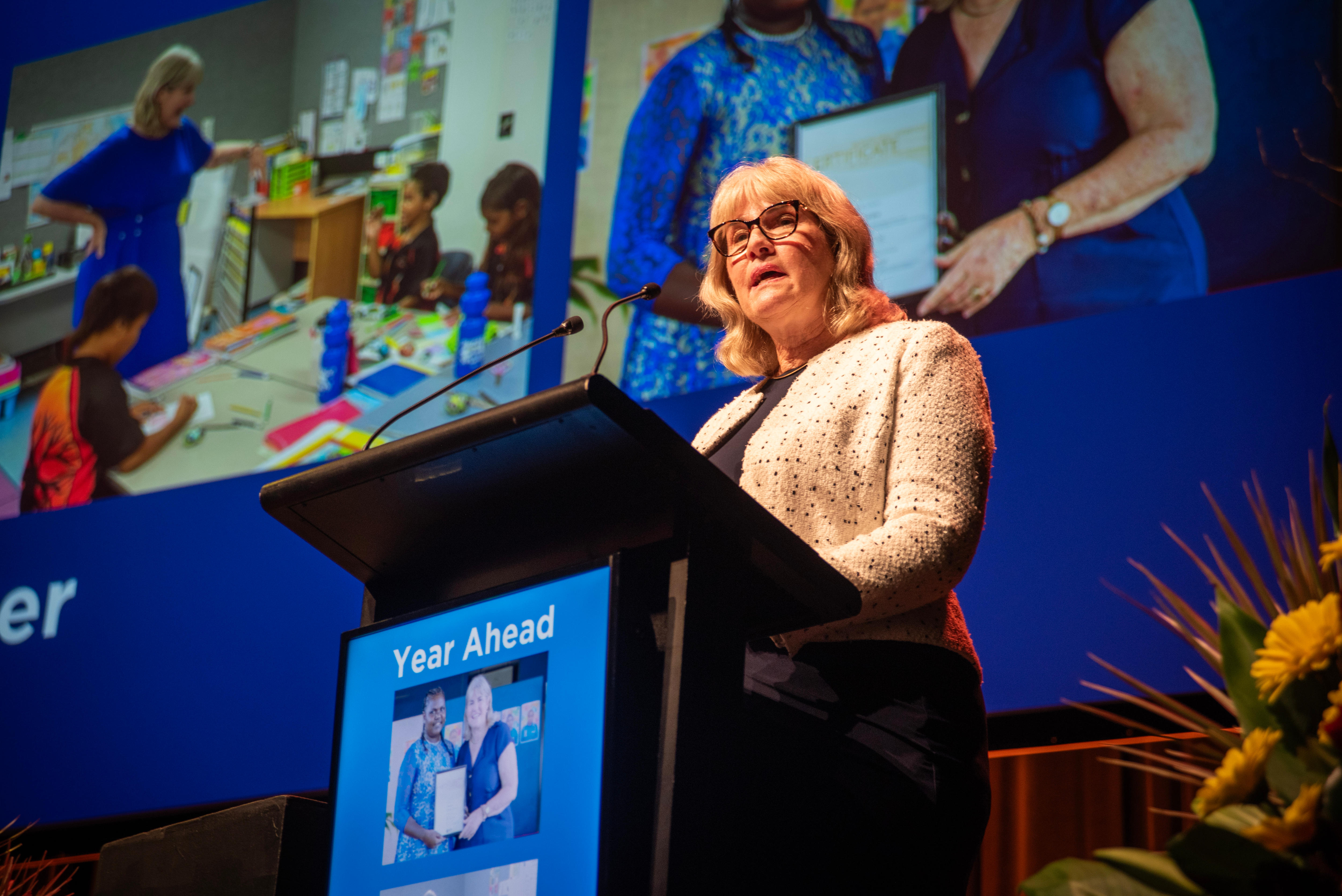Eva Lawler stands behind a podium talking on stage. She has a serious expression.