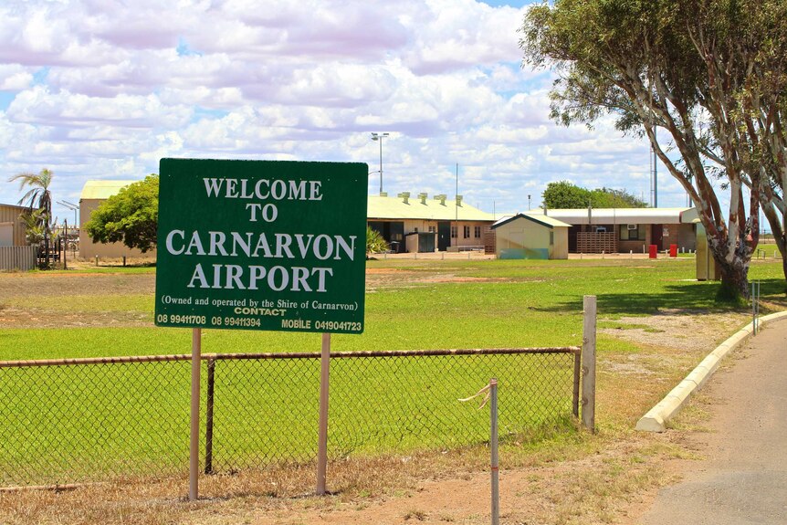A sign in front of a rural airfield that reads "Carnarvon Airport".