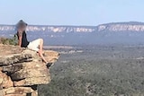 Man sits on the edge of a sandstone cliff at Boolimba Bluff, Carnarvon Gorge.