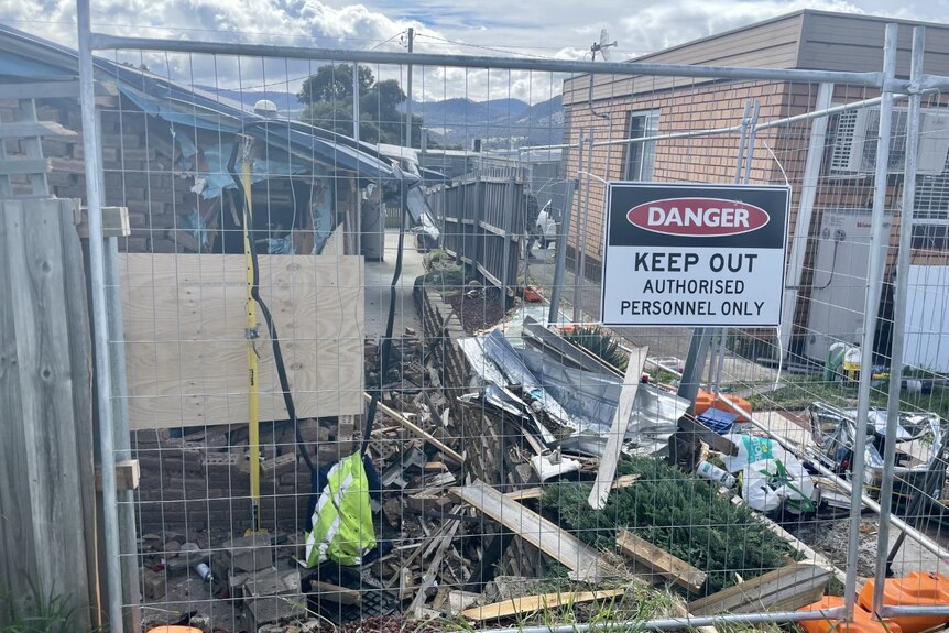 Damage outside a house with a fence bearing a "keep out" sign.